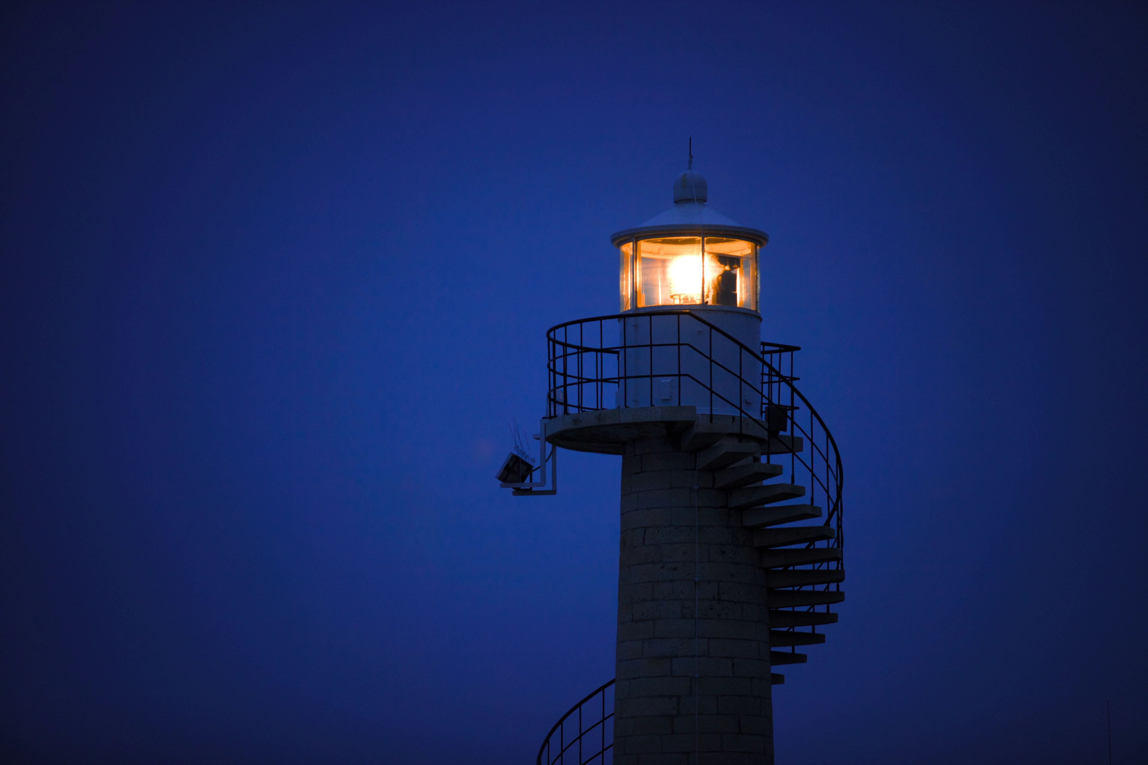 A lighthouse lit at blue hour against a deep blue sky
