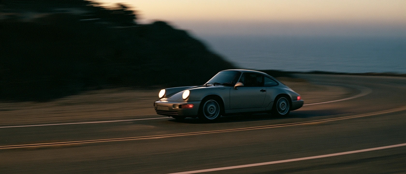 A classic Porsche 911 on a winding coastal road at dusk